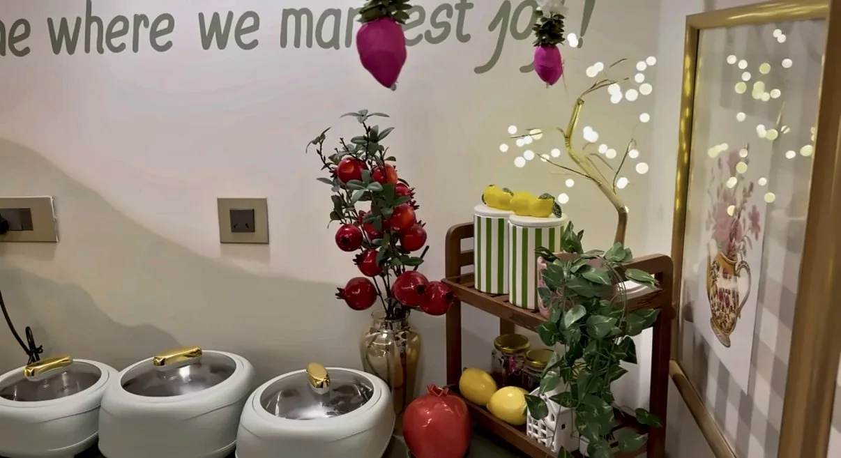 Pomegranate stems in a glass vase beside a gold light tree and a wooden two-tier shelf