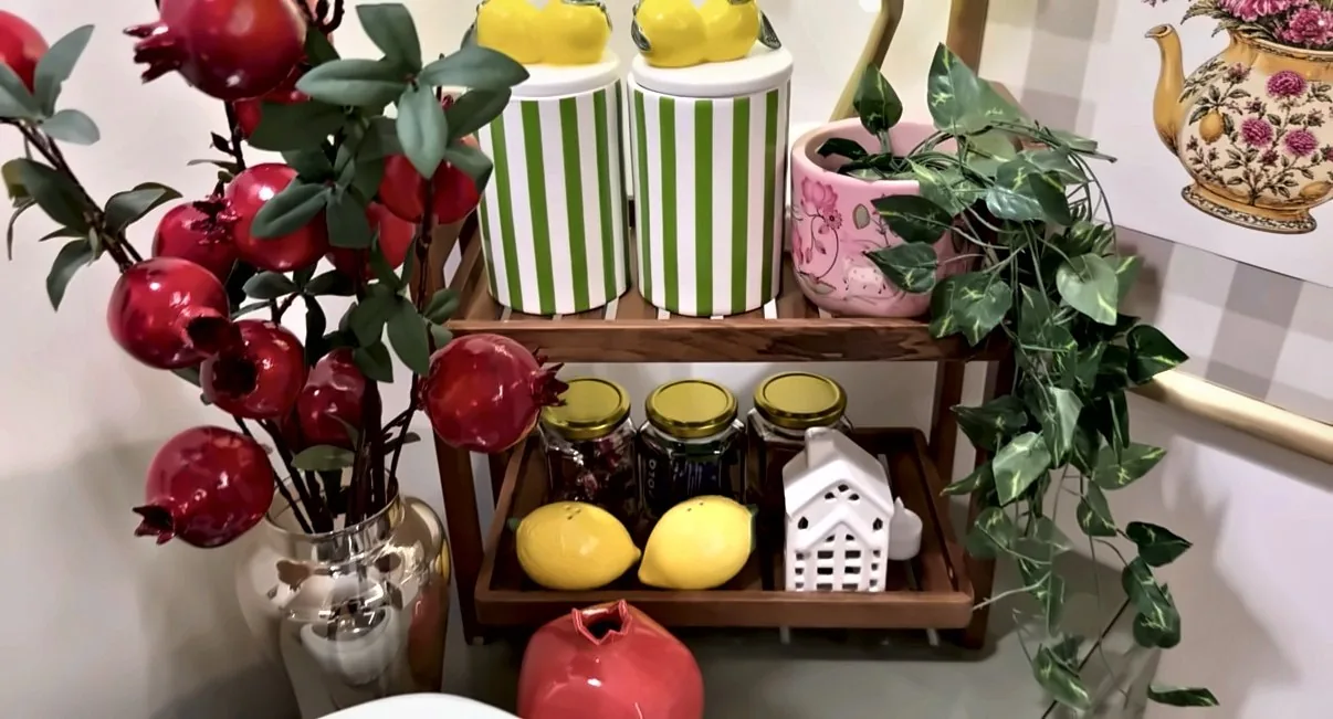 Two-tier wooden shelf with striped lemon-lid jars, glass jars, ceramic lemons, a white house lantern and a pink planter