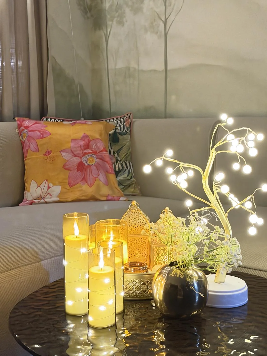 Flameless pillar candles, a pearl bonsai tree light and gold lanterns on a coffee table