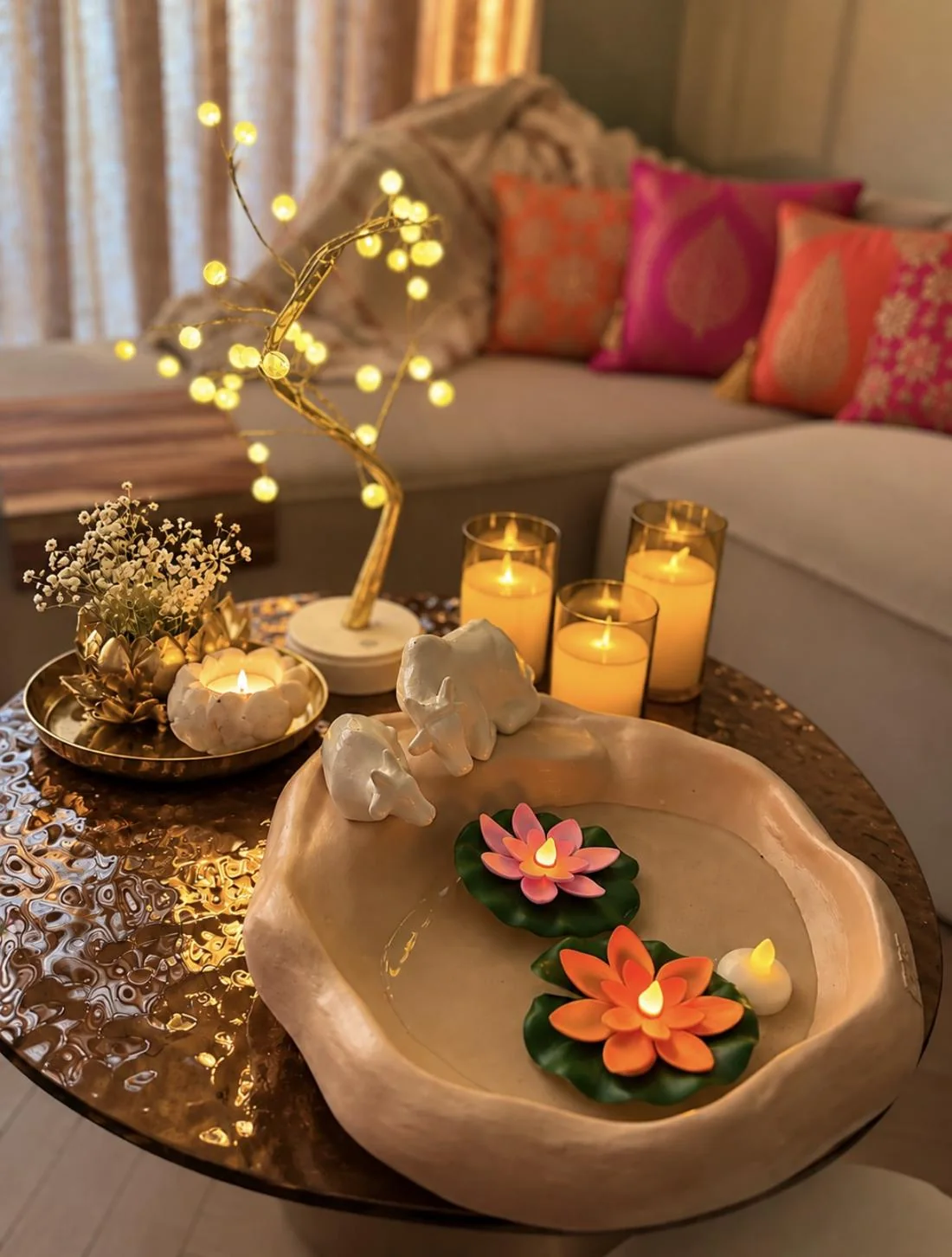Floating lotus LED candles in a ceramic urli beside a pearl tree lamp and flameless pillar candles