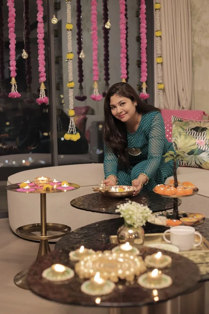 Sitting by the coffee table with a pooja thali, pink and marigold hangings behind