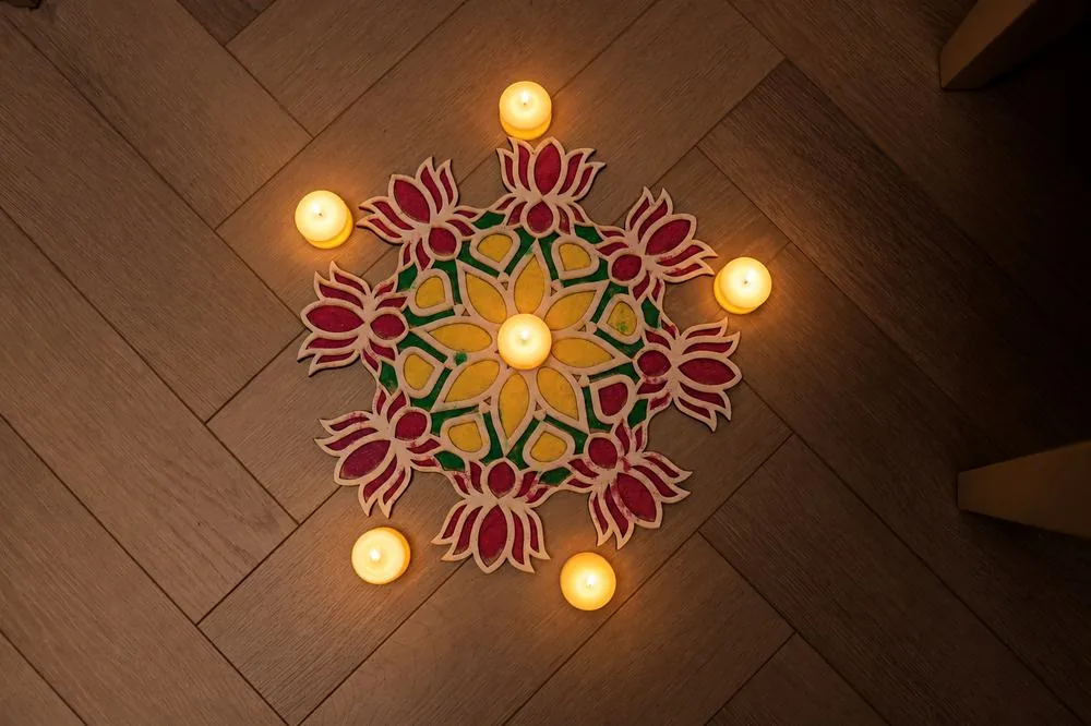 Wooden-floor rangoli stencil in red, yellow and green ringed with candles
