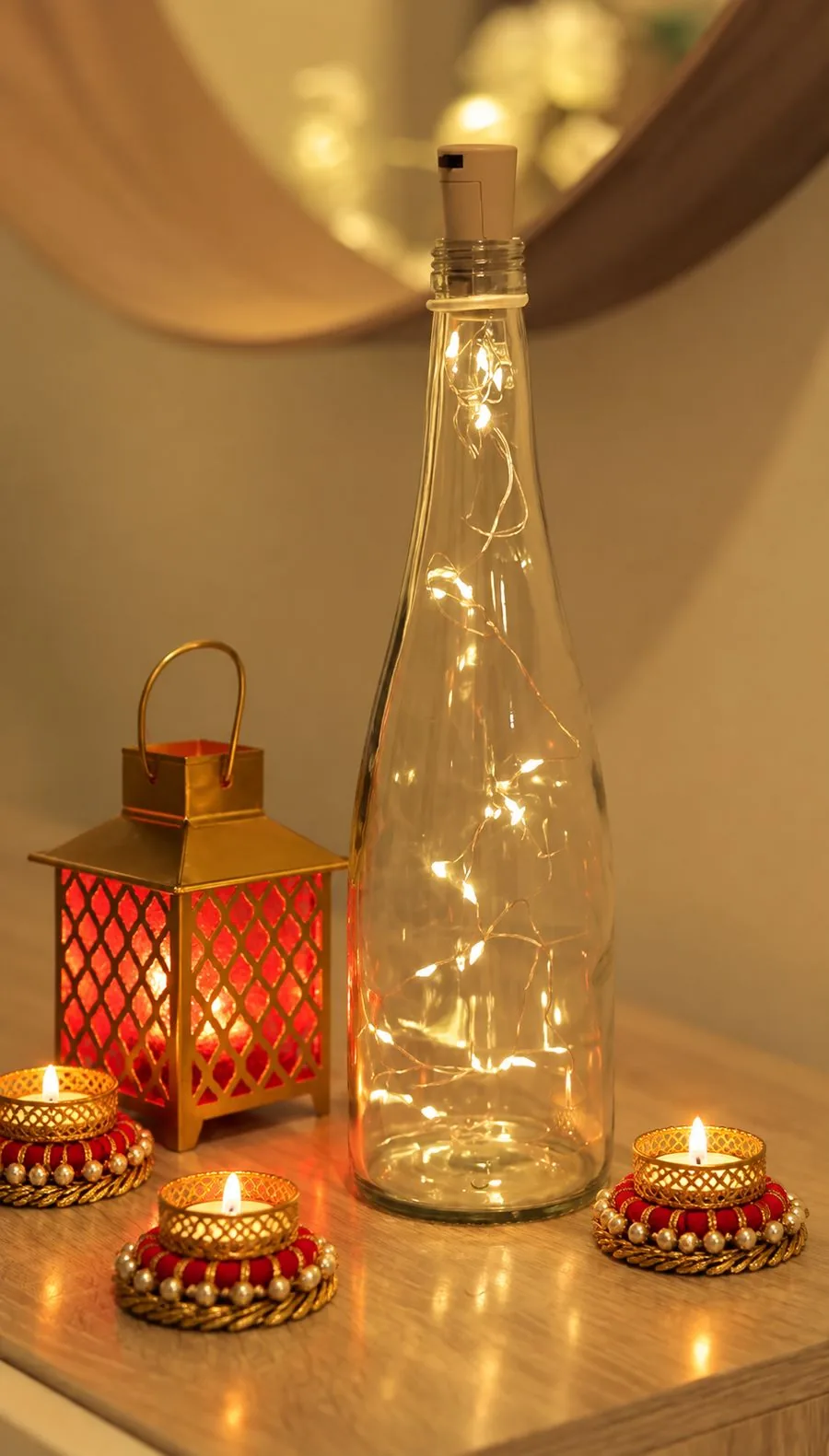 A red glass lantern and pearl tealight holders beside a bottle of fairy lights