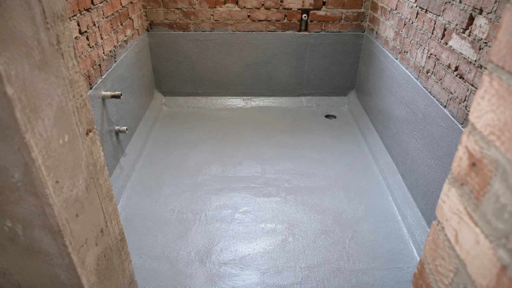 A bathroom floor and lower walls coated grey with waterproofing membrane, brickwork still exposed above
