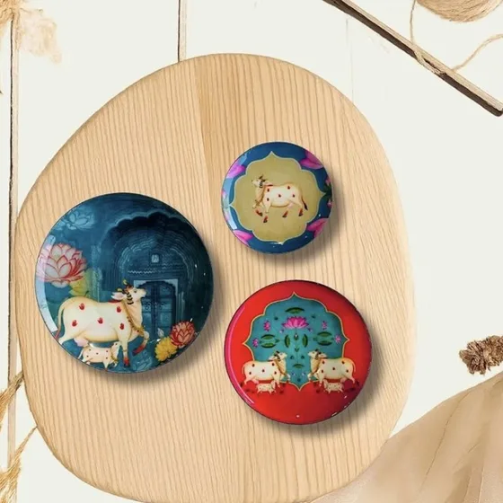 Round Pichwai-painted plate magnets with cow motifs, on a wooden board