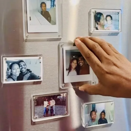 A hand placing clear acrylic photo frame magnets on a steel fridge door