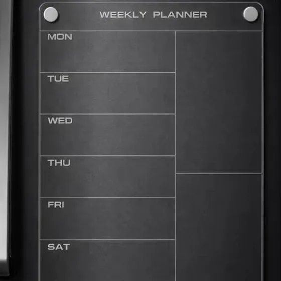 A clear weekly planner board with Monday to Saturday rows on a black fridge door