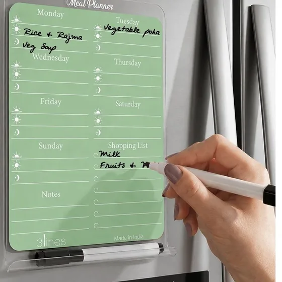 A green acrylic meal planner board on a fridge, with a hand writing on it in marker
