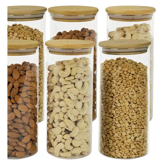 Six tall glass jars with bamboo lids, filled with almonds, cashews and peanuts
