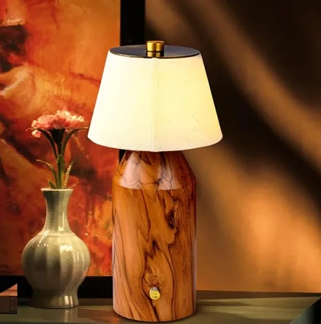 A cordless lamp with a turned wooden body and a cream fabric shade, lit on a side table