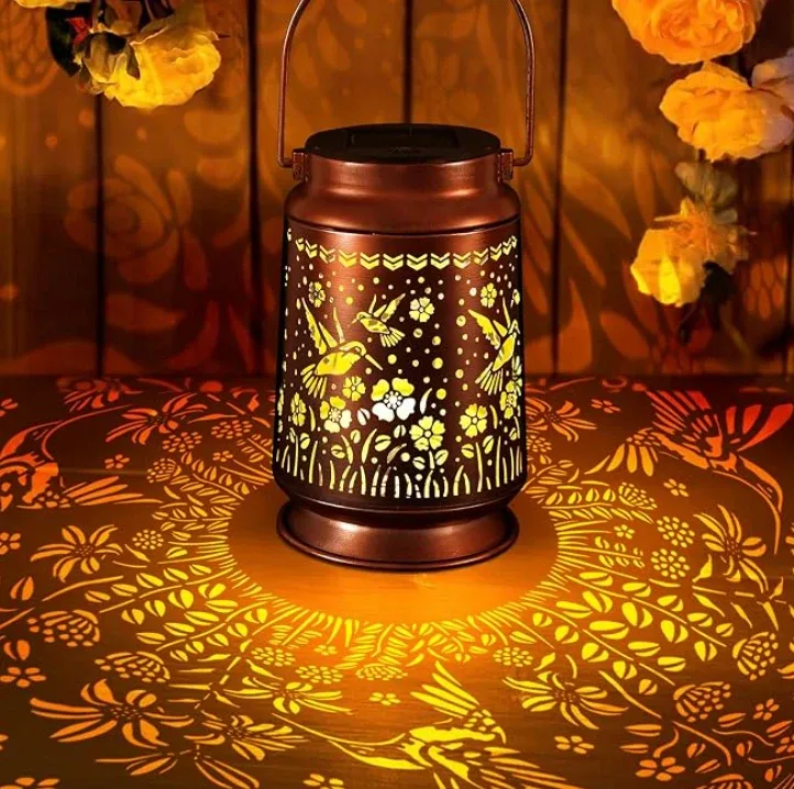 A copper solar lantern with cut-out birds and flowers, throwing that pattern across the table