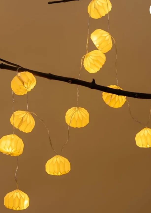 Folded paper lanterns strung along a bare branch, glowing warm