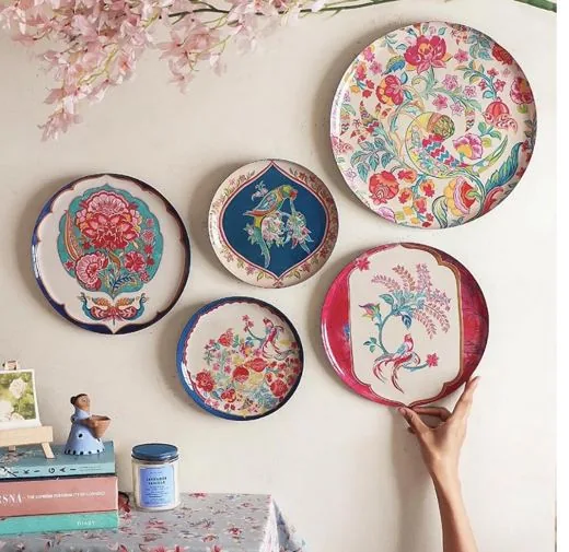 Five hand-painted floral wall plates in pink, blue and cream, hung in a cluster