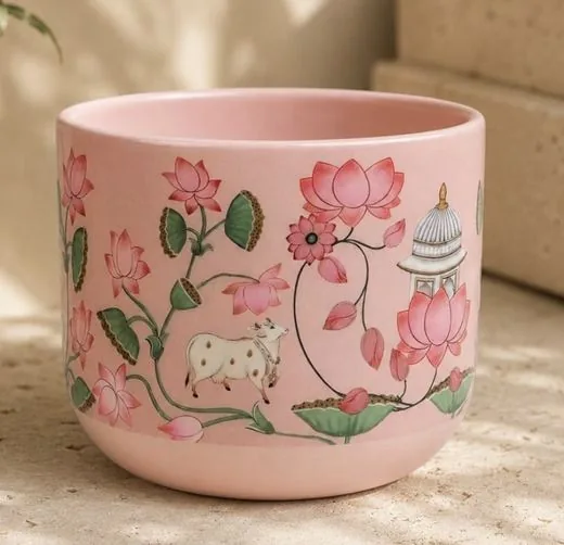 A pink ceramic planter painted with Pichwai lotuses and a cow