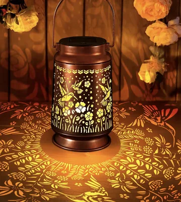 Copper solar lantern with cut-out hummingbirds casting patterns of light