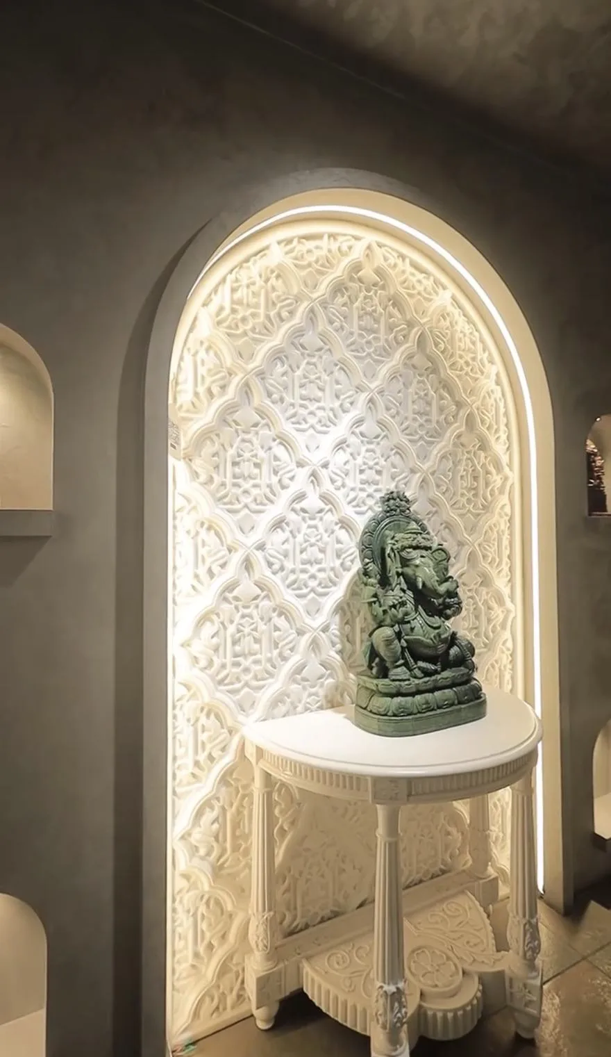 Arched niche filled with a carved white marble jaali panel, lit from behind, with a carved marble side table